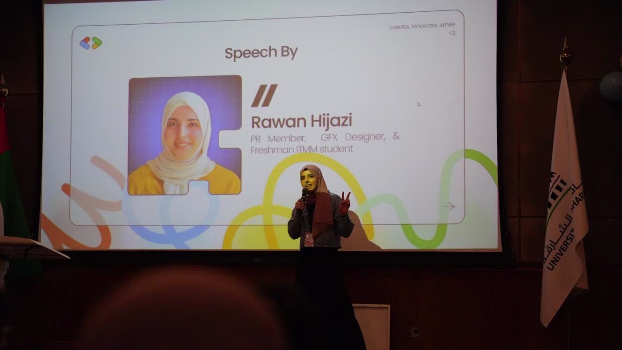 Rawan in a hijab holding a microphone and giving a speech in front of a presentation slide that shows her photo and name, Rawan Hijazi, with the description 'PR Member, GFX Designer, & Freshman ITMM student'.